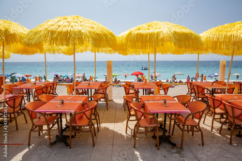 Yellow umbrellas and cafe tables line the Menton promenade facing the beach