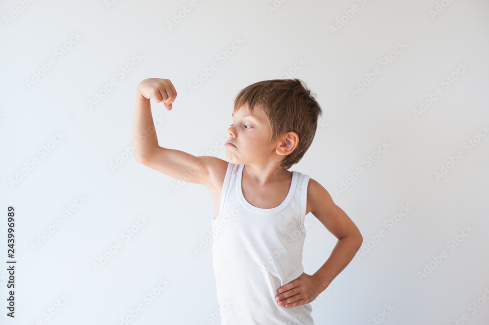 strong small child in white tank top showing his muscle with grimace on his face strong small child in white tank top showing his muscle with grimace on his face
