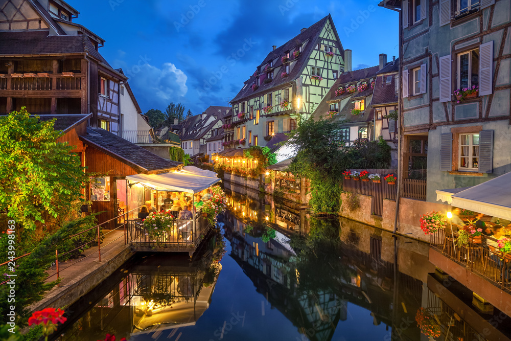 Colmar, France. Half-timbered houses and verandas of restaurants reflecting in the water at dusk in Petite Venise area