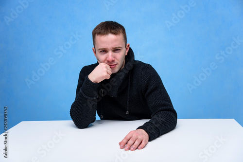 Concept studio portrait of a young man on a blue background sitting on a cube.