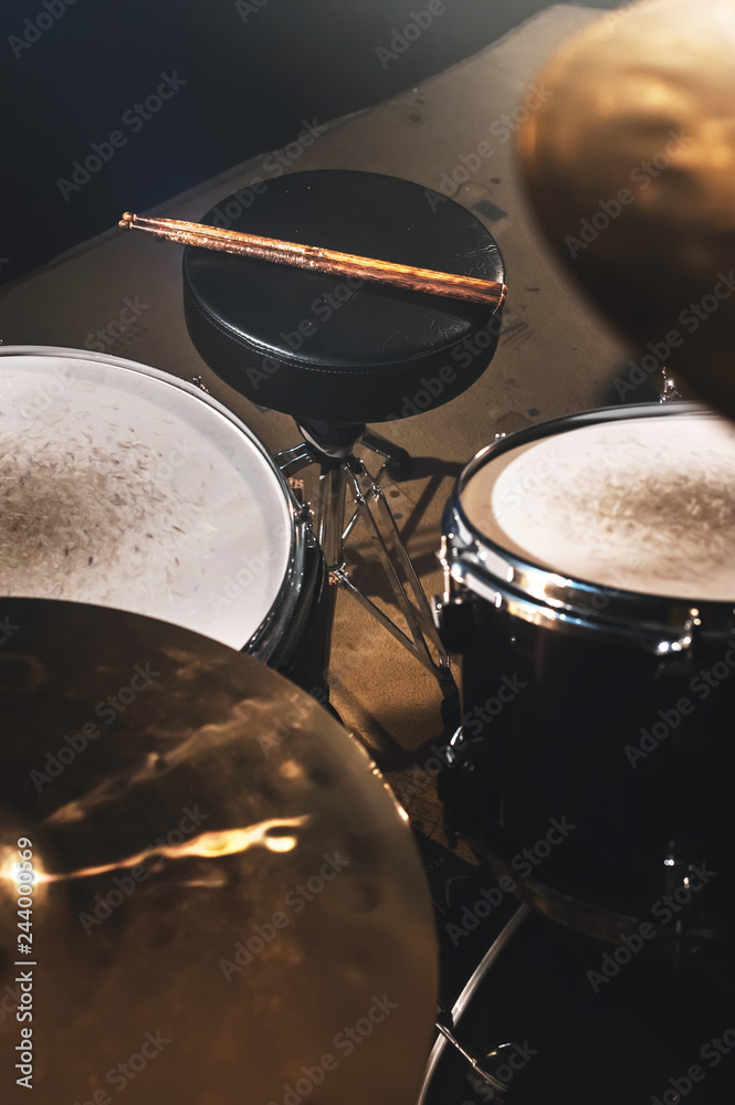 Closeup view of a drum set and Drumsticks in a dark studio. Black drum barrels with chrome trim. The concept of live performances Closeup view of a drum set and Drumsticks in a dark studio. Black drum barrels with chrome trim. The concept of live performances