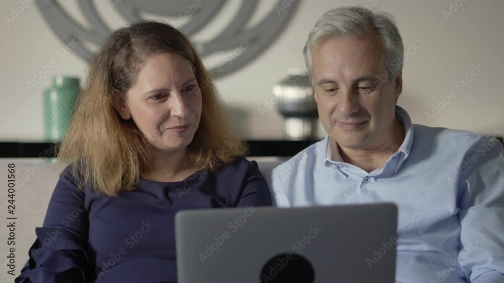 Couple of parents talking to adult children. Middle aged man and woman sitting on couch and using laptop for video call. Distance communication concept Couple of parents talking to adult children. Middle aged man and woman sitting on couch and using laptop for video call. Distance communication concept