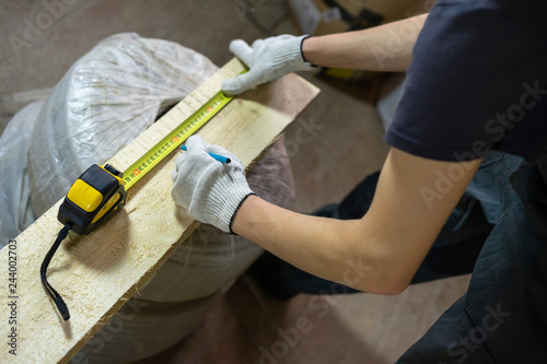 Close-up. A young man makes repairs in the house. Measures a wooden board with a ruler.