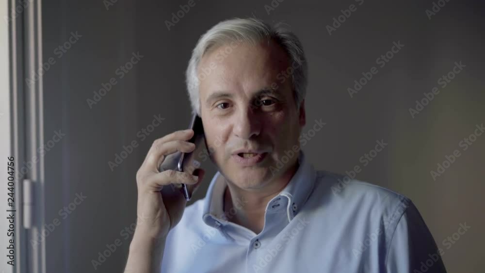 Positive middle aged man discussing on cell something funny. Front view of cheerful phone user talking on smartphone indoors. Phone talk concept Positive middle aged man discussing on cell something funny. Front view of cheerful phone user talking on smartphone indoors. Phone talk concept
