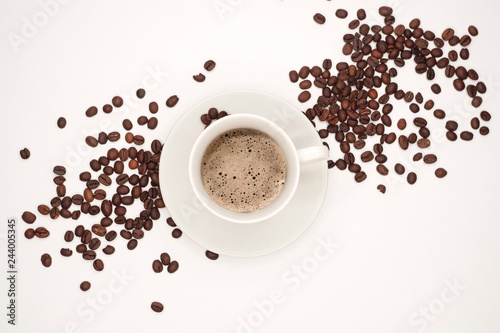 White cup with black classic coffee and a saucer among coffee grains. Top view, isolated on white background