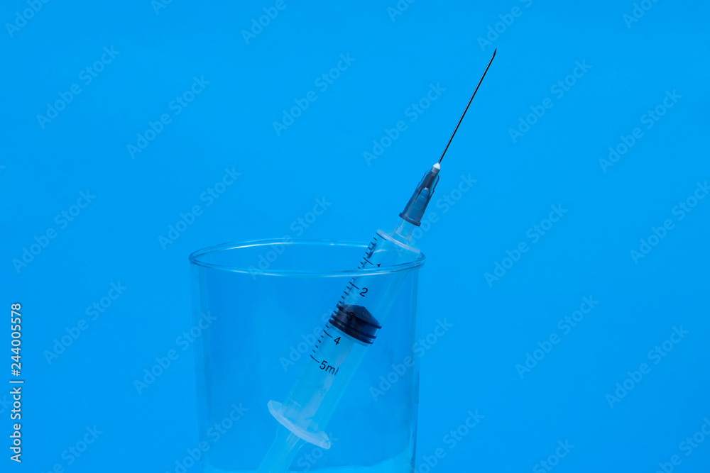 syringe in a glass on a blue background, laboratory syringe in a glass on a blue background, laboratory