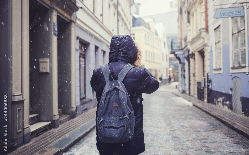 man with a backpack walks through the old town of Riga in the winter