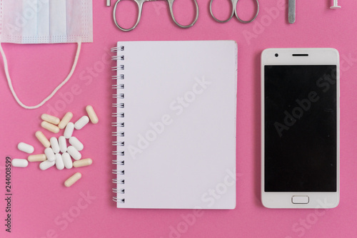on the pink surface lie a white smartphone, notebook, pills and medical dental instruments