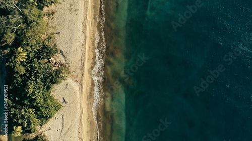 stunning aerial drone minimal geometric image of a remote tropical sea ocean shore with sandy beach lush rainforest jungle and crystal clear azure blue water from top looking down at sunset