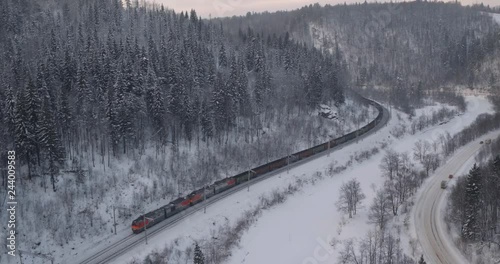 Freight train with coal on Trans Siberian winding two-sided railways near river at winter frozen day in Ural Mountains in Russia - Aerial top view