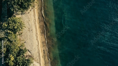 stunning aerial drone minimal geometric image of a remote tropical sea ocean shore with sandy beach lush rainforest jungle and crystal clear azure blue water from top looking down at sunset