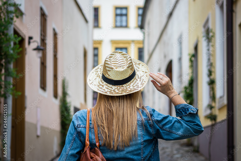 Woman wearing denim jacket and straw hat. Female tourist walking in the city streets