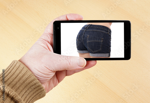 male hand holding smart phone showing sexy photo of female butt in hot pants photo