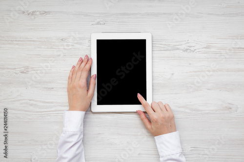 Female hands using tablet on a white wooden surface, top view. From above, overhead, flat lay.