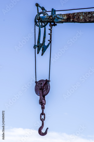 Close up view of hook crane for lifting boats and cargo. Blue sky background.