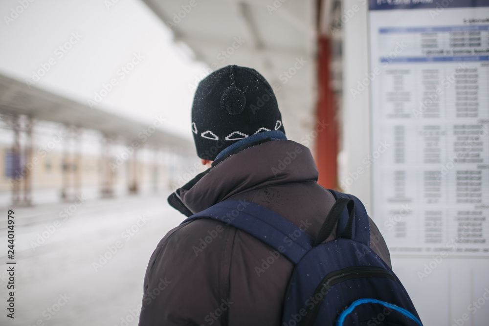 man traveler studies standing on the railway platform and studying the train schedule in winter man traveler studies standing on the railway platform and studying the train schedule in winter