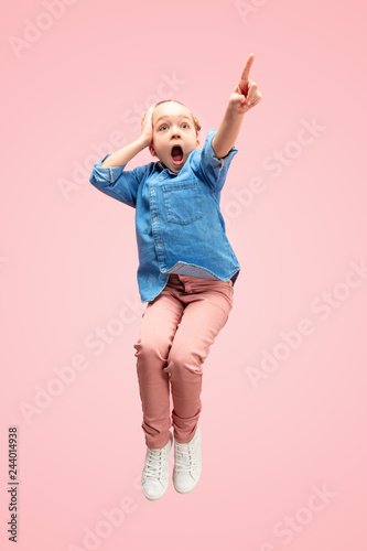 Young happy surprised caucasian teen girl jumping in the air, isolated on pink studio background. Beautiful female full length portrait. Human emotions, facial expression concept.