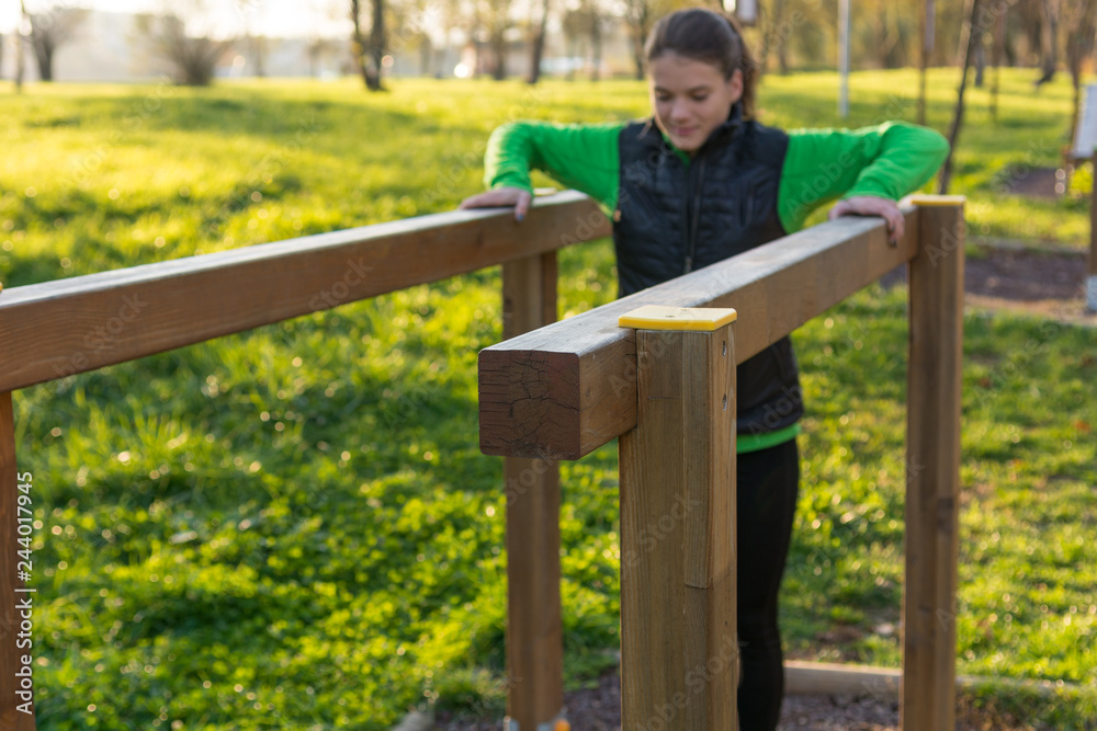 Athletic female doing leg raises on wooden beams outdoor.