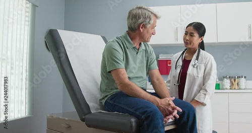 Japanese woman doctor talking to senior Caucasian male patient in exam room