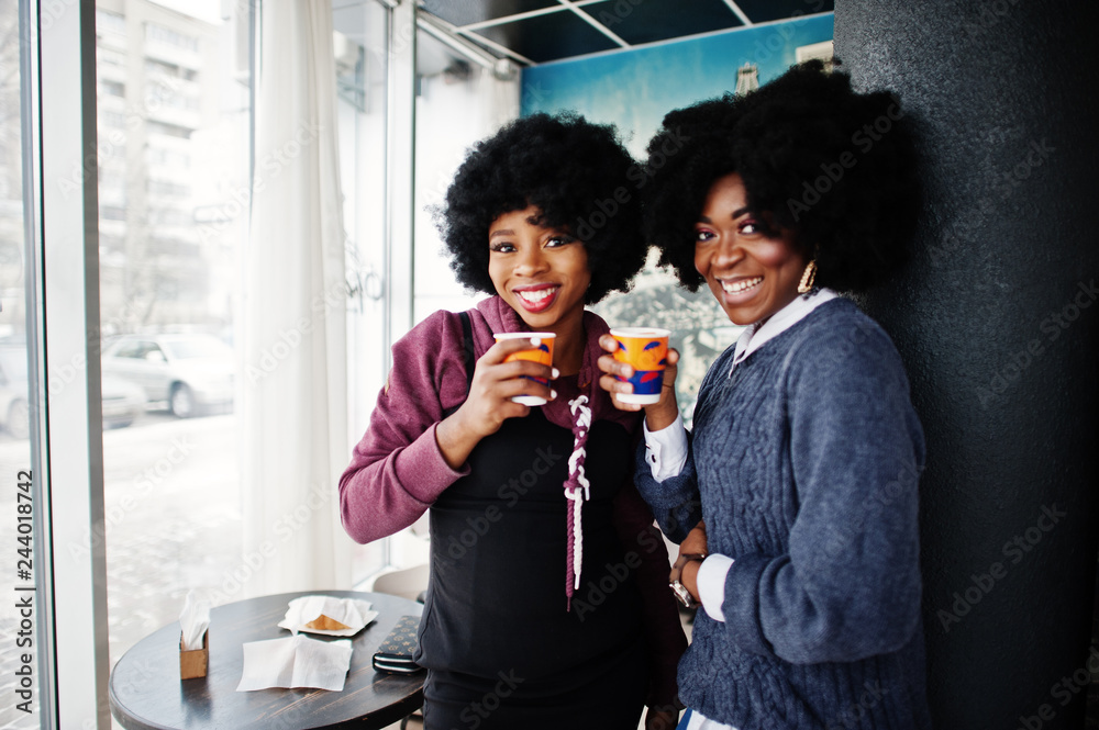 Two curly hair african american woman wear on sweaters with cups of tea posed at cafe indoor. Two curly hair african american woman wear on sweaters with cups of tea posed at cafe indoor.