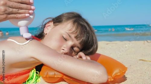 Spread sunblock on the body. Mother smears sunscreen on the back of a little girl on a sunny day at the beach.