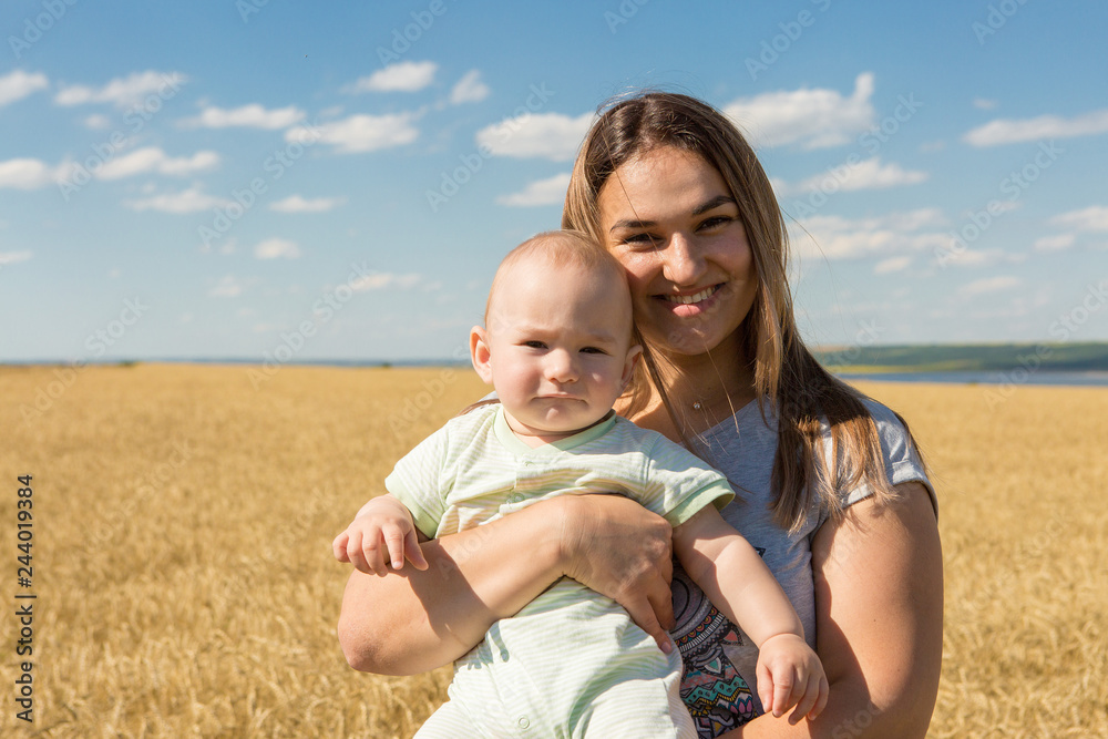 Fototapeta premium Mother with child in wheat, Young happy family in wheat field smiling and enjoying the sun