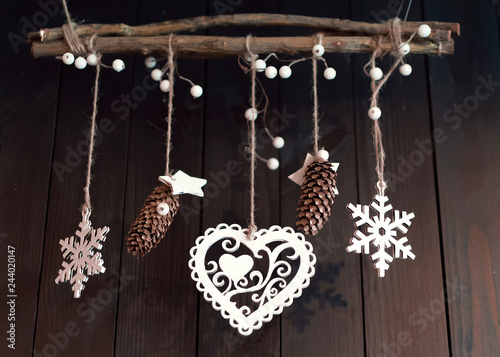 Christmas decor on a wooden brown wall background. Cones, heart, berries and stars hanging on the ropes on the branch.