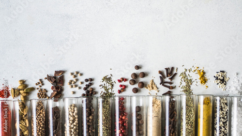 Various dry spices in glass tubes and spilled on gray background. Copy space. top view
