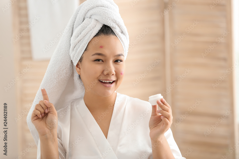 Portrait of young Asian woman with acne problem and jar of cream in bathroom