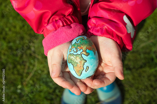 Fototapeta Naklejka Na Ścianę i Meble -  Child holding an egg with Planet Earth painted on it on a sunny day outdoors