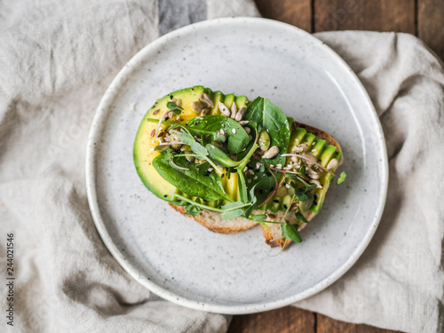 Green healthy sandwich made from spinach, sprouts, avocado and various seeds on a white plate on a wooden background. top view