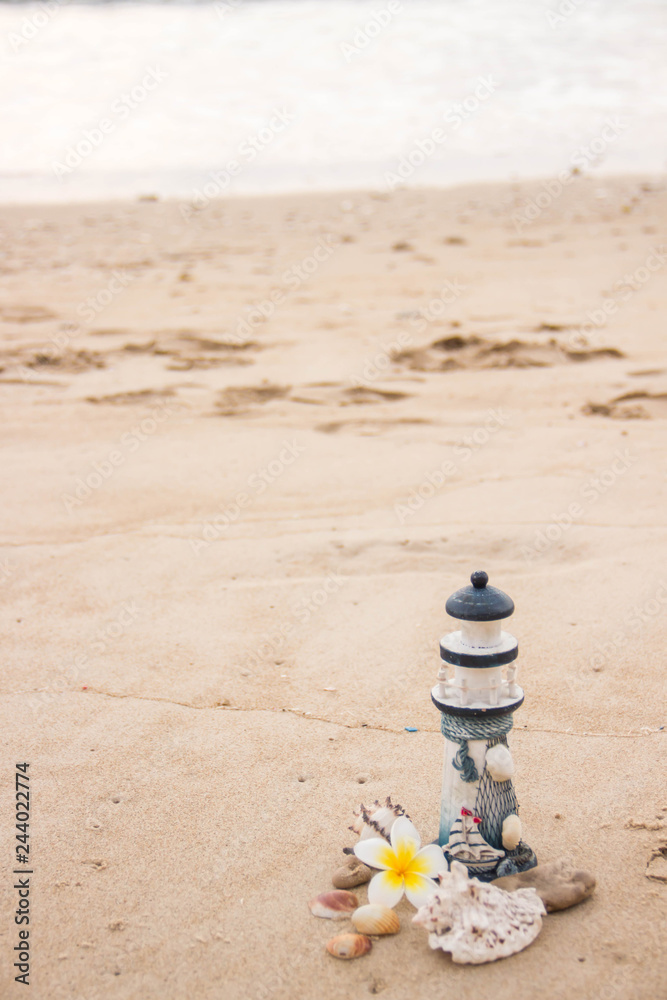 A small decorative lighthouse with a magnolia flower and shells is laid out on the sand overlooking the sea with a place for an inscription. A small decorative lighthouse with a magnolia flower and shells is laid out on the sand overlooking the sea with a place for an inscription.