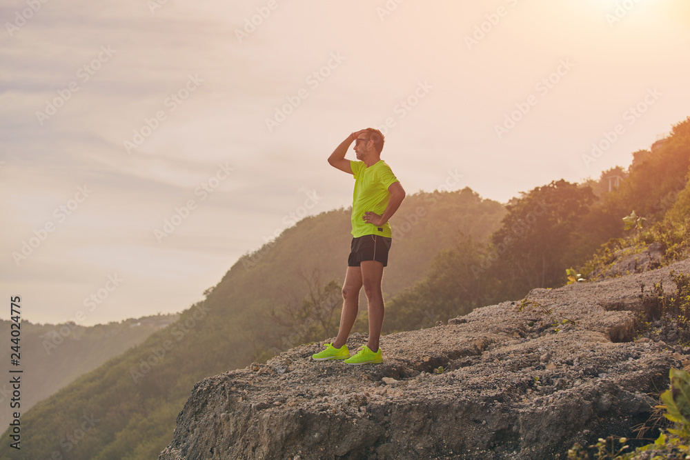 Sportsman making pause after workout on a tropical cliff.