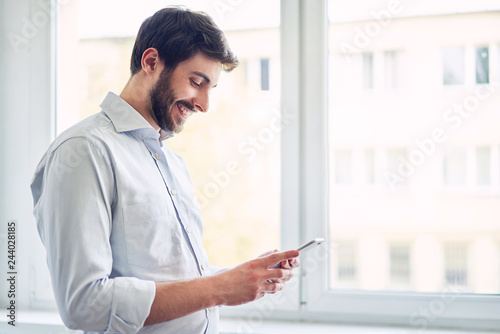 Young man using smartphone and laughing at office