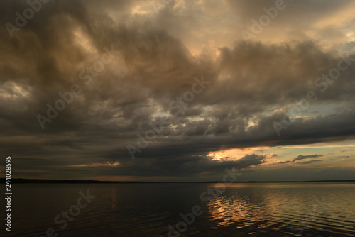 Rays of sunlight from a dark cloud in a cloudy sky above the quiet water surface of a lake