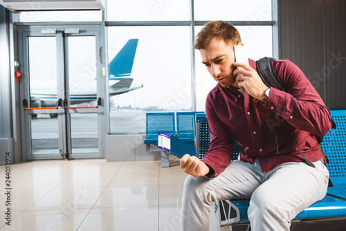 man talking on smartphone while sitting in waiting hall