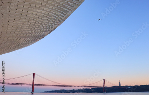 The MAAT - Museum of Art, Architecture and Technology with a Airplaine arriving to lisbon with the 25 of april bridge in background at the sunset. Lisbon Portugal