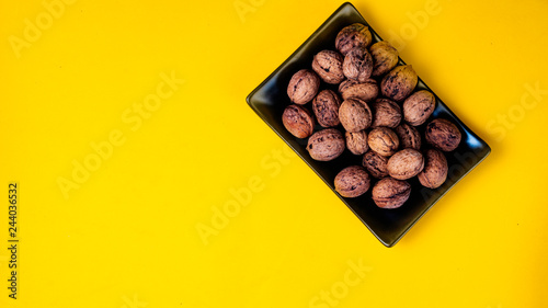 Black plain dish full of nuts on a yellow background. © Sergi