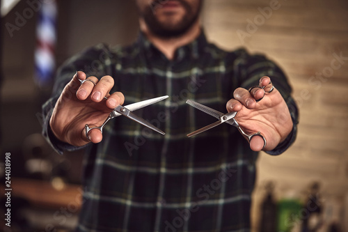 Man hairdresser in a plaid shirt holding a sharp professional scissors. Close-up