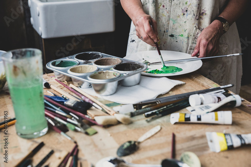 High angle close up of artist mixing green and brown colours on white plate. photo