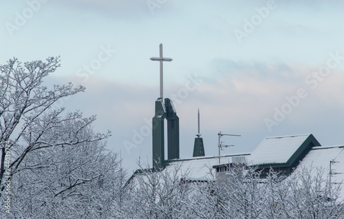 The cross of the Catholic Church looks out from behind snow-covered trees on a cloudy day