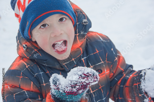 A little boy is eating snow. The child eats cold snow.