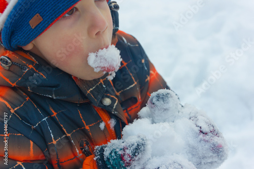 A little boy is eating snow. The child eats cold snow.