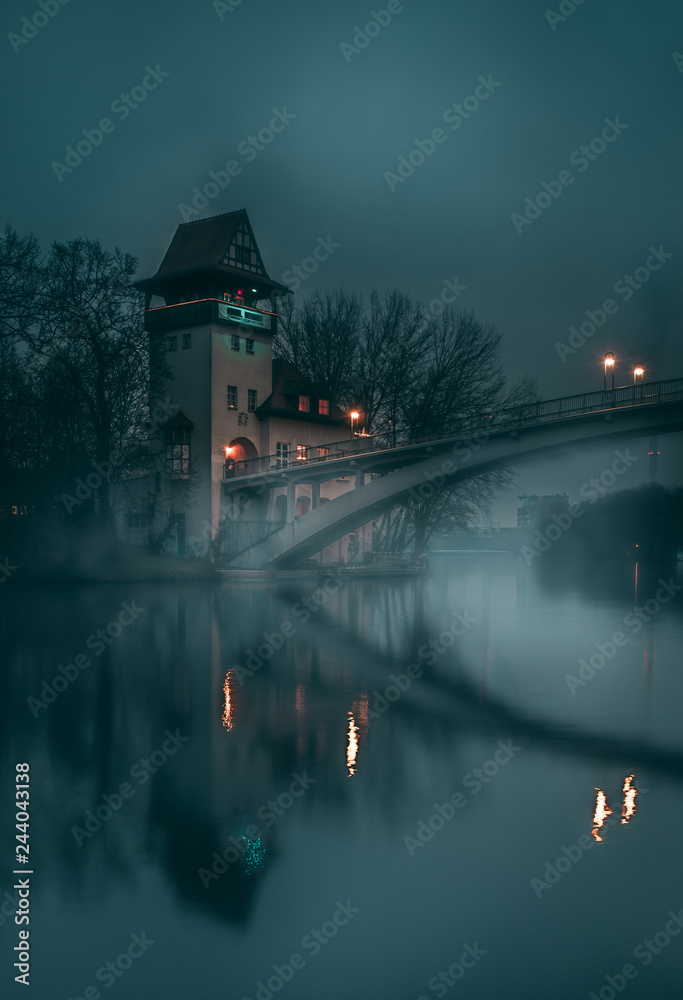 Scenery of the island of youth and its pedestrian bridge and tower at riverside along Spree river located in the Treptower park after sunset at night, during winter season in Berlin, Germany.