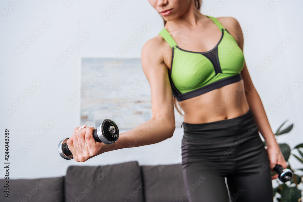 cropped view of sportswoman exercising with dumbbells at home cropped view of sportswoman exercising with dumbbells at home