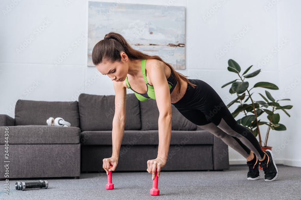focused sportswoman doing push ups with dumbbells at home focused sportswoman doing push ups with dumbbells at home