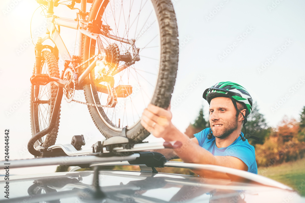 Fototapeta premium Cyclist man hold on his bike on the car roof