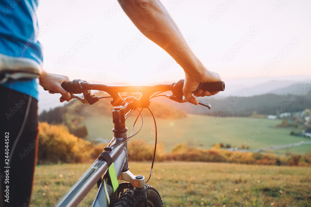 Fototapeta premium Man with bike stay on the top of hill and enjoying the sunset. Man hands on the bike steering wheel close up image