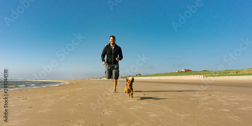 Man with his little cute dog running at the beach photo