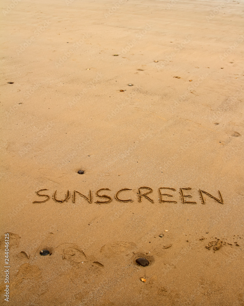 Fototapeta premium The word sunscreen drawn in sand at the beach with copy space